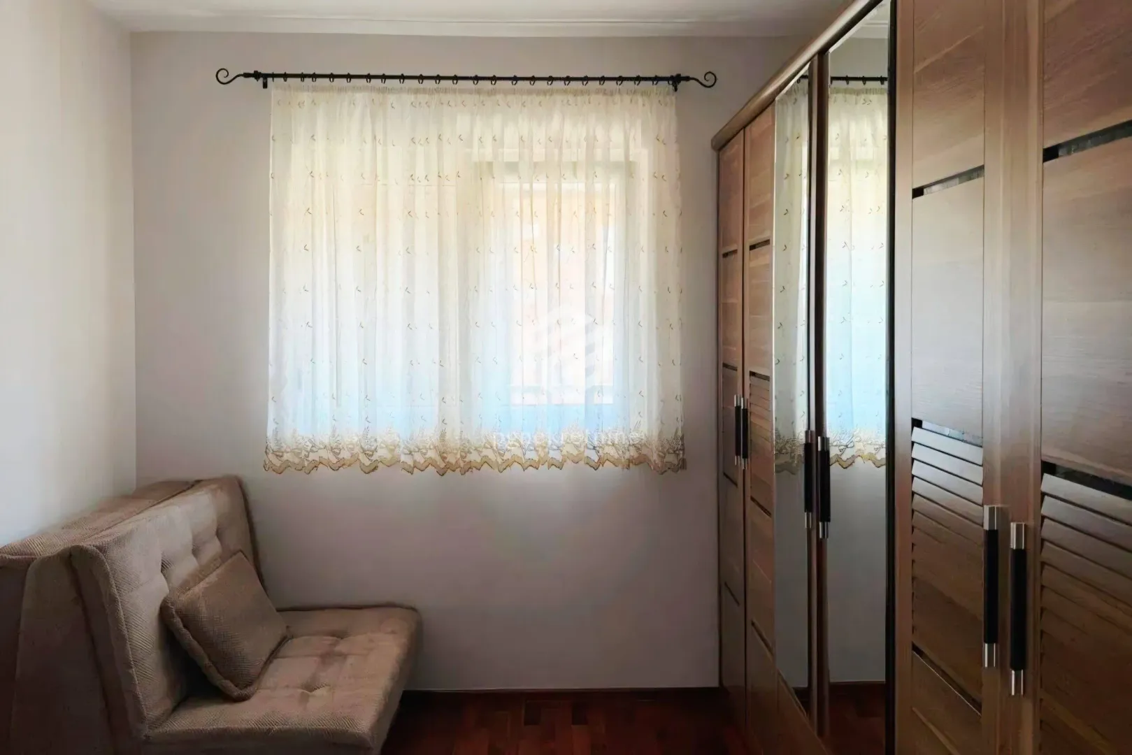Bedroom with a bed, a window with curtains, and wooden wardrobes.