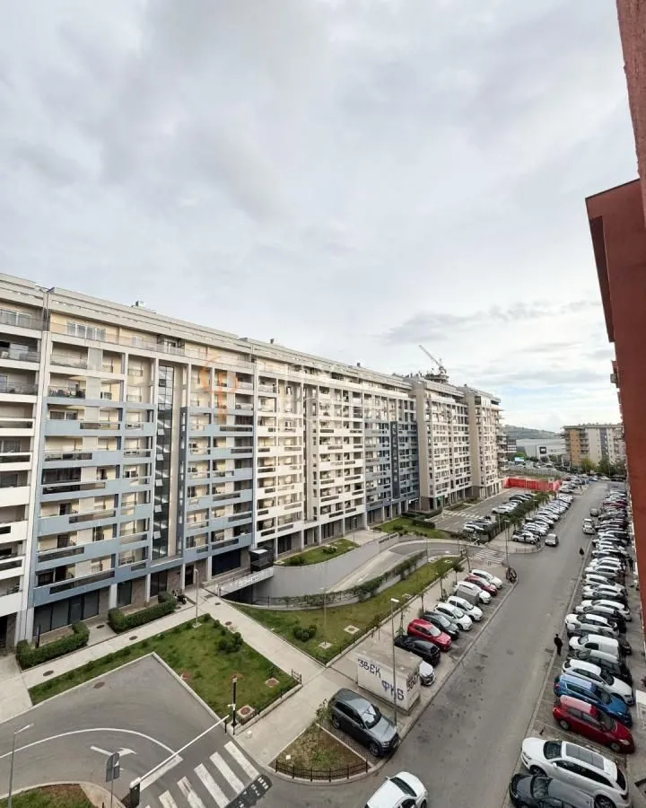 Pogled sa terase na stambenu zgradu i parking ispred objekta.