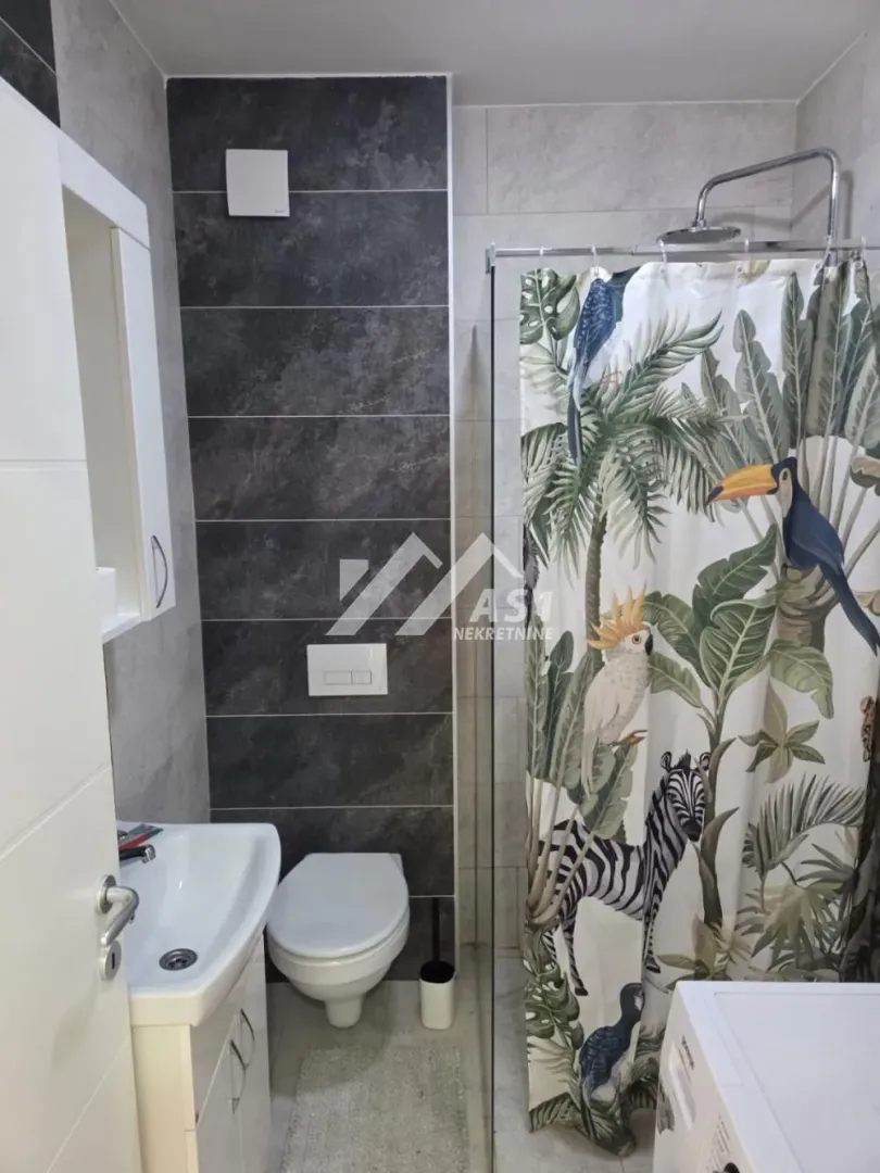 Bathroom equipped with a washbasin, toilet, and a shower cabin with a decorative curtain.