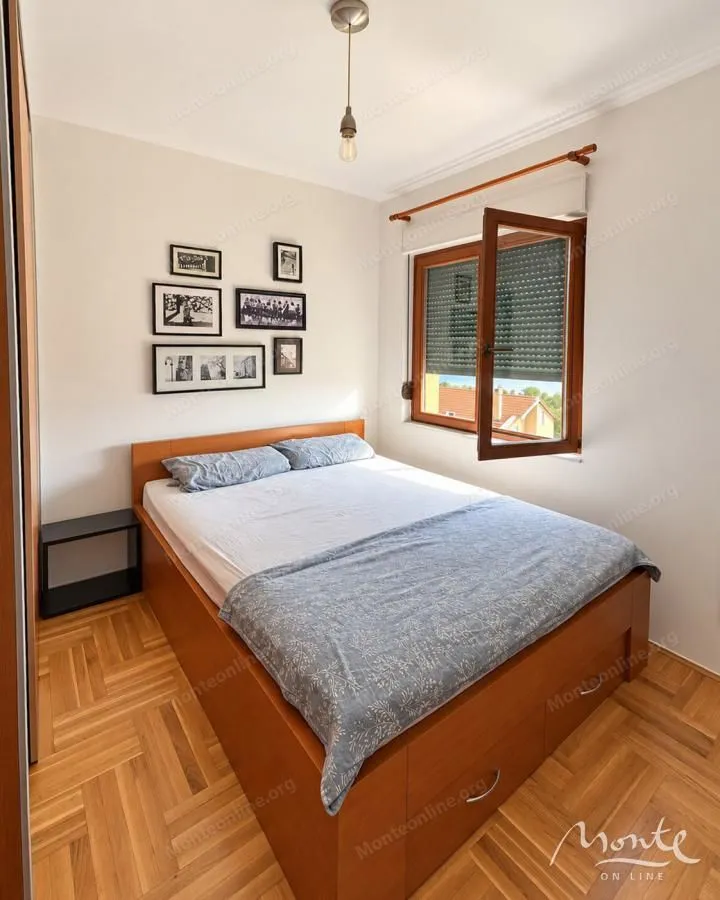 Manja spavaća soba sa bračnim krevetom, drvenim podom i prozorom.