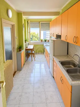 Dugačka kuhinja sa narandžastim elementima i trpezarijskim kutkom pored prozora. - image 3