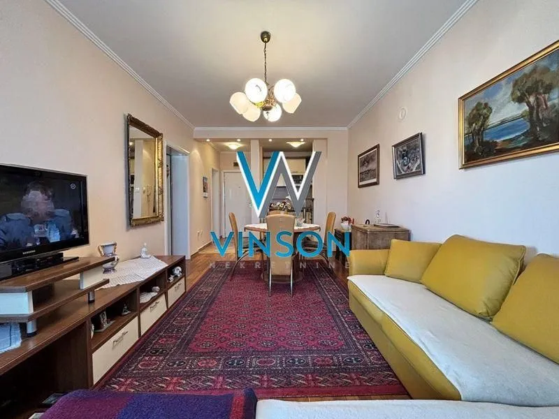 Dnevna soba sa garniturom, televizorom i trpezarijskim delom u pozadini.
