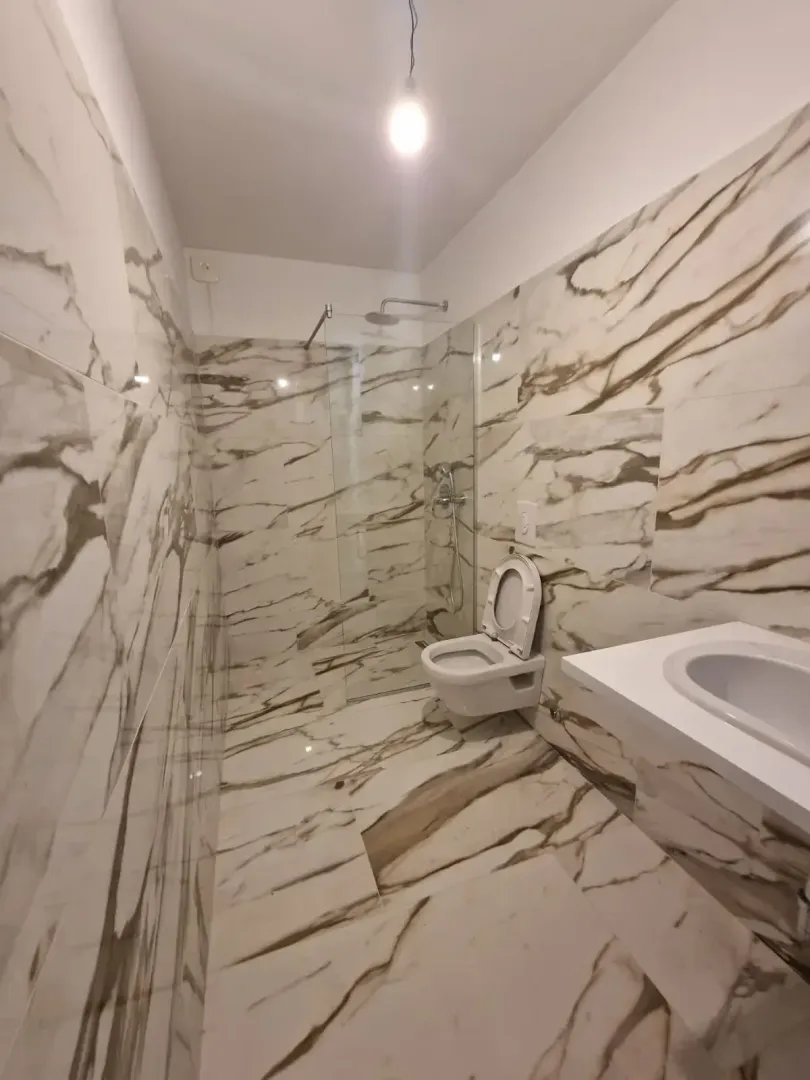 Bathroom tiled in marble-pattern tiles with a walk-in shower and washbasin.