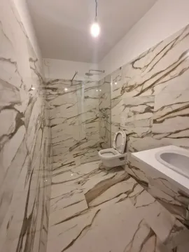 Bathroom tiled in marble-pattern tiles with a walk-in shower and washbasin. - image 10