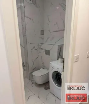 Pogled na kupatilo sa keramičkim pločicama, toaletom i veš mašinom. - image 9