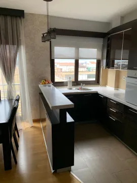 Kuhinja sa tamnim elementima, šankom i trpezarijskim stolom pored prozora. - image 6