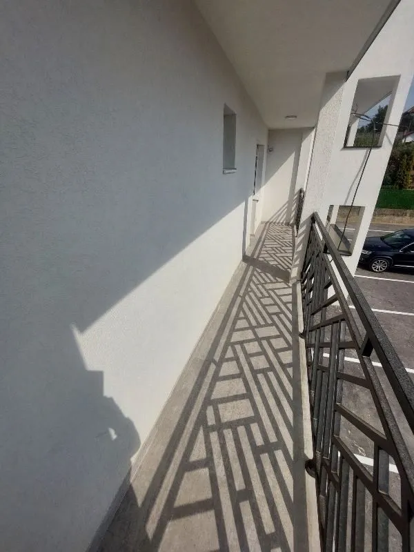 Dugački balkon sa metalnom ogradom i pogledom na dvorište i parking.