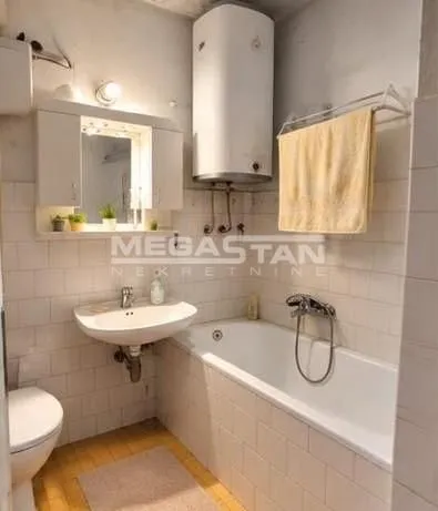 Smaller bathroom equipped with a bathtub, washbasin, toilet, and water heater.