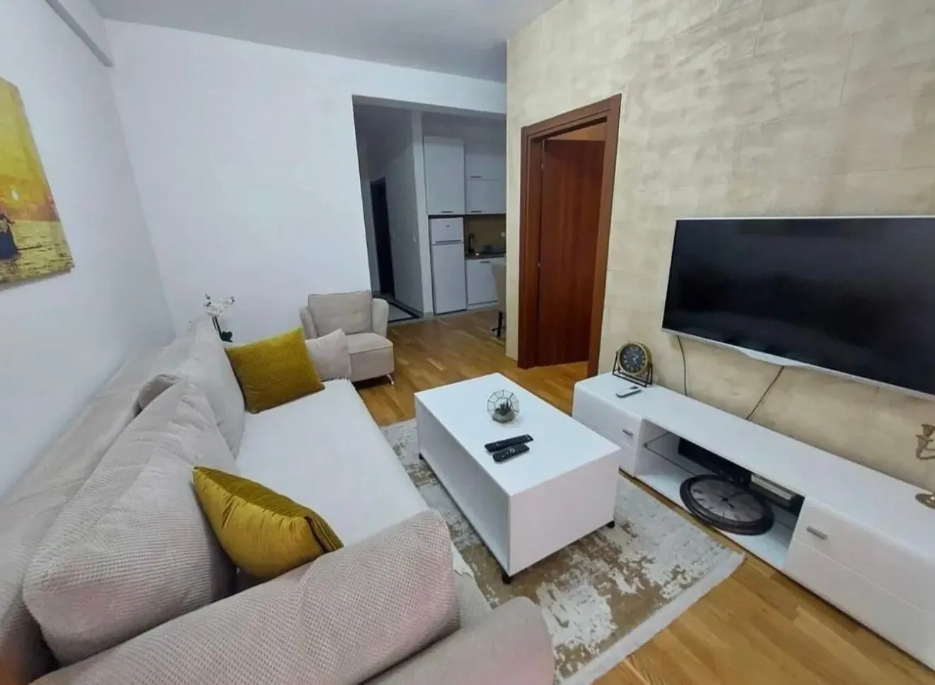 Namještena dnevna soba sa garniturom, TV-om i pogledom na kuhinju.