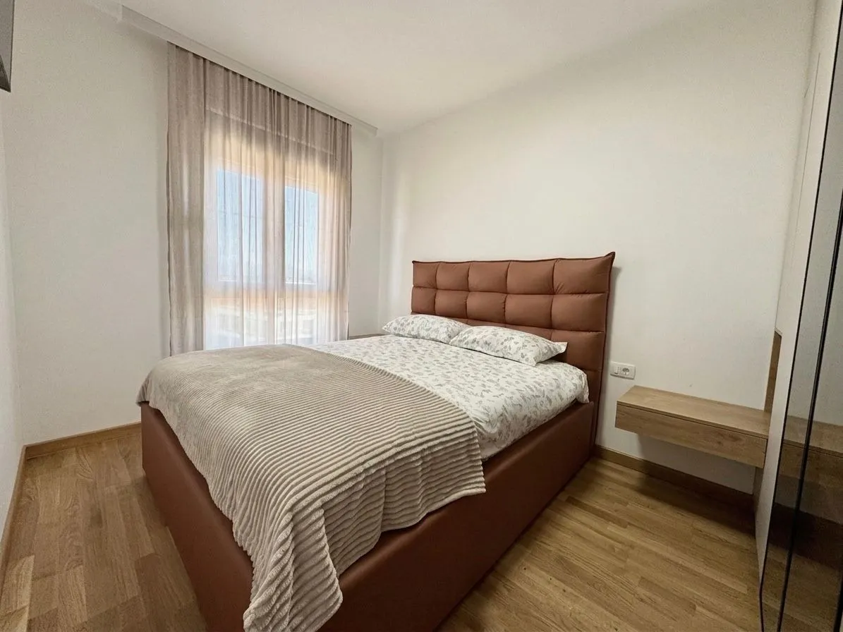 Namještena spavaća soba sa bračnim krevetom i prozorom sa zavjesama.