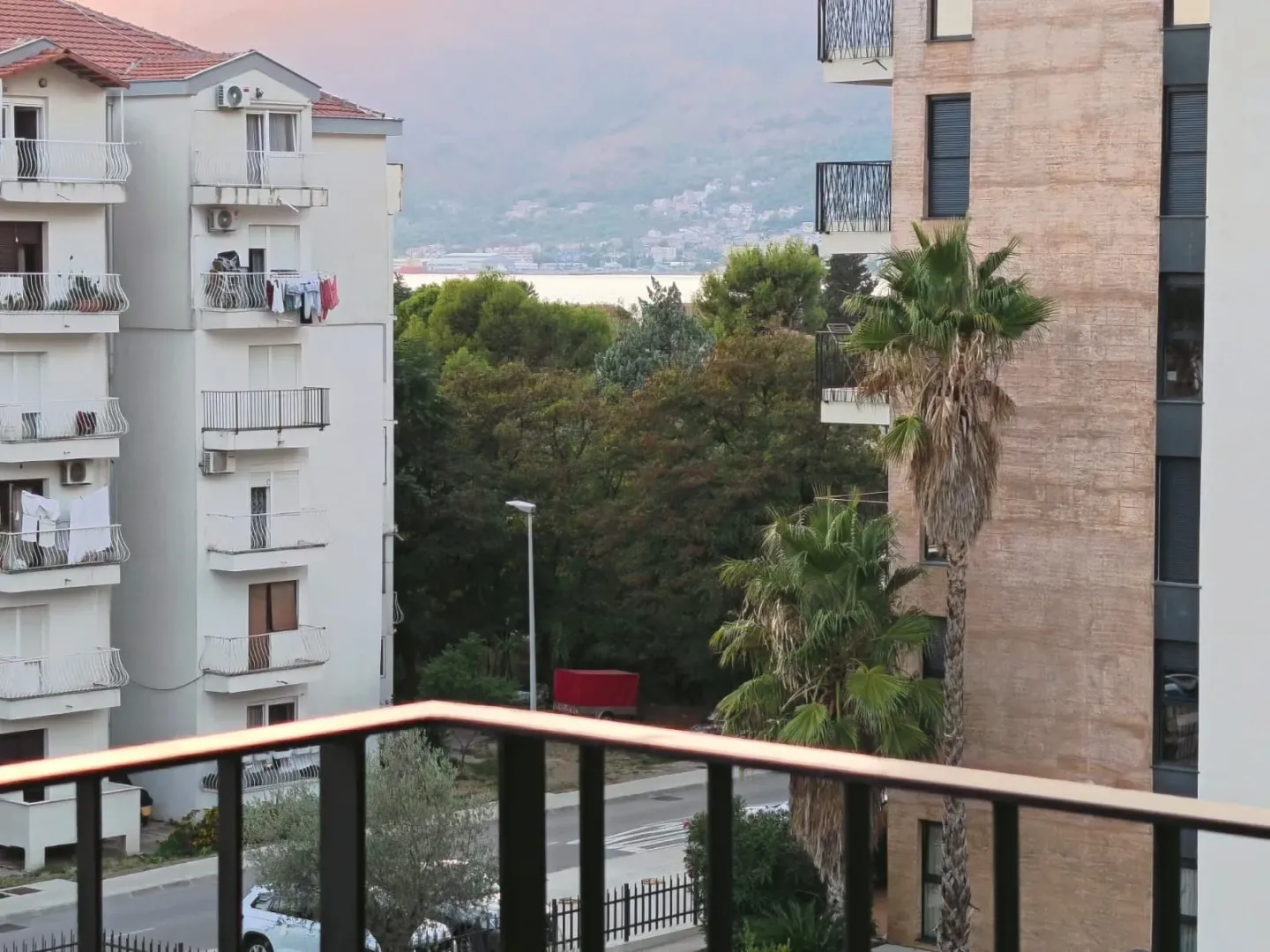 View from the terrace towards the surrounding buildings, greenery, and the sea in the distance.