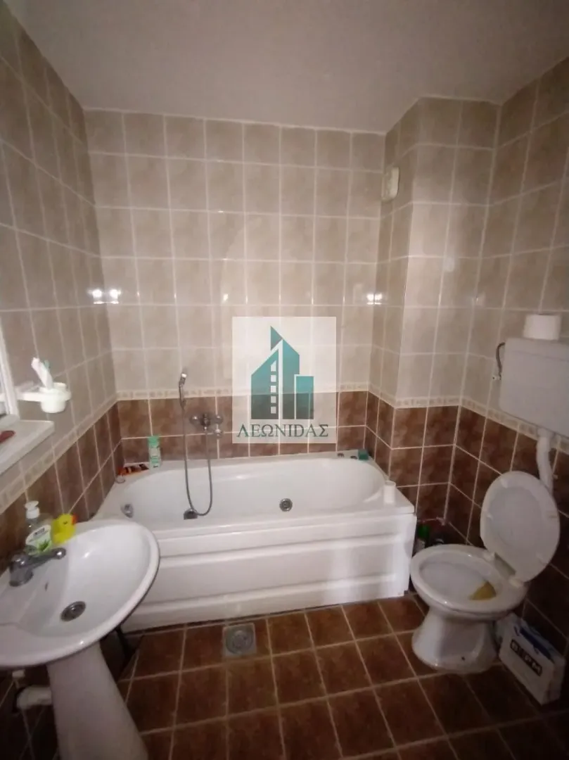 Bathroom equipped with a bathtub, washbasin, and toilet featuring ceramic tiles on the walls and floor.