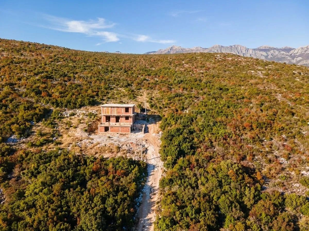 Pogled iz vazduha na nedovršenu kuću u prirodi okruženu rastinjem i planinama.