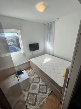Mala spavaća soba sa krevetom, zidnim televizorom i prozorom. - image 6