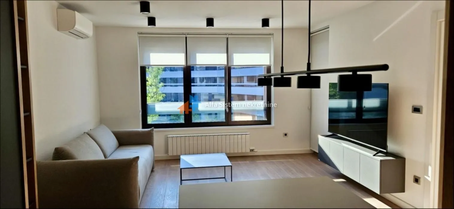 Dnevna soba sa garniturom, TV-om i velikim prozorom.