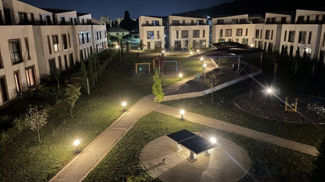 Noćni pogled na osvijetljeno dvorište i fasadu stambenog kompleksa.