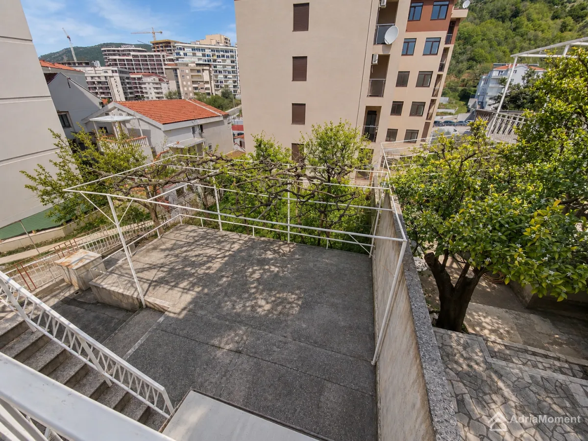 Velika popločana terasa sa pergolom i pogledom na okolne zgrade i zelenilo.