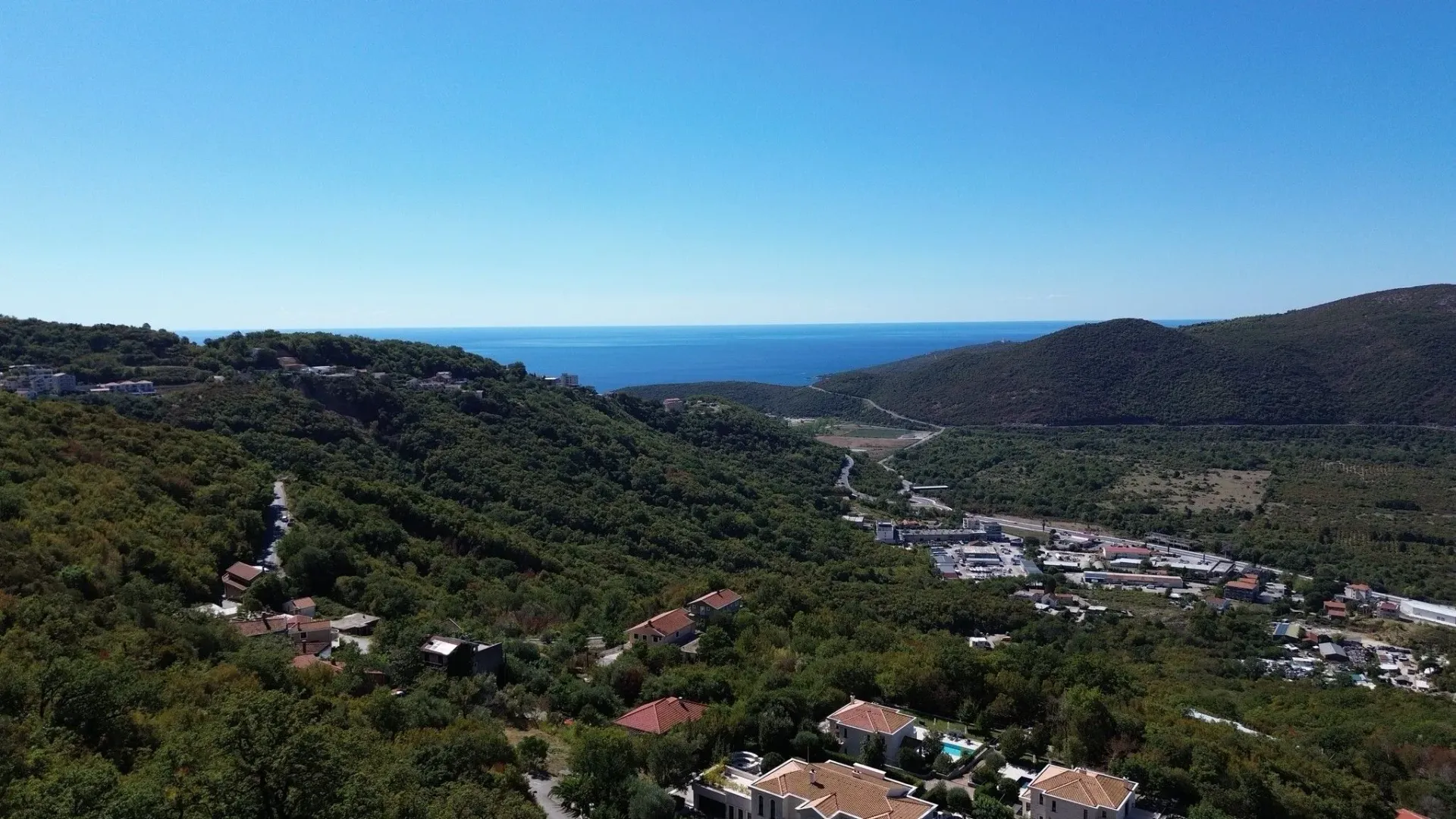 Pogled iz vazduha na prirodu, naselje i more u daljini.