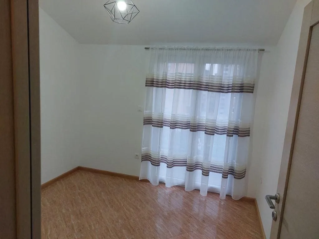 An empty room with white walls, a window with curtains, and tiled flooring.
