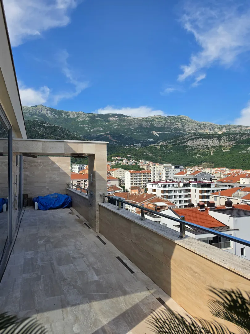 Prostrana popločana terasa sa pogledom na grad i planine.