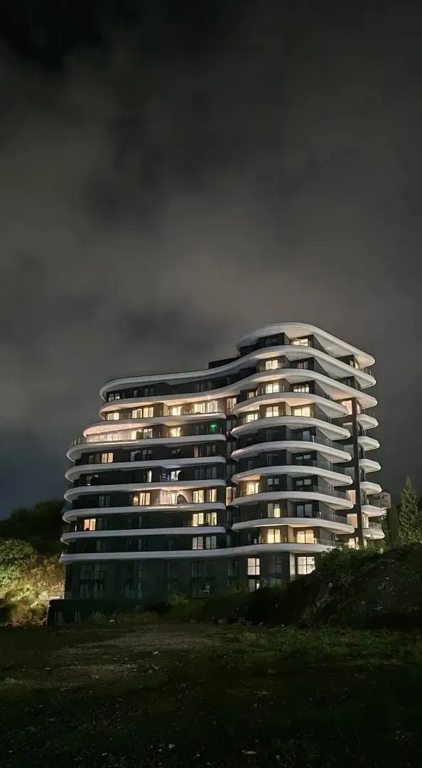Noćni pogled na modernu stambenu zgradu sa osvijetljenim terasama.