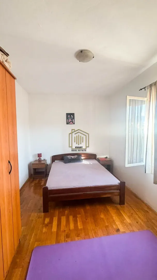 Spavaća soba sa bračnim krevetom, drvenim podom, ormarom i prozorom.