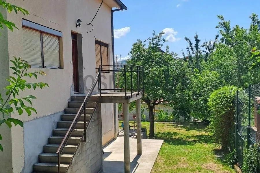 Eksterijer kuće sa spoljnim stepeništem, balkonom i dvorištem sa zelenilom.