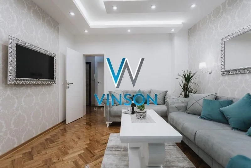 Dnevna soba sa garniturom, stočićem i televizorom na zidu.