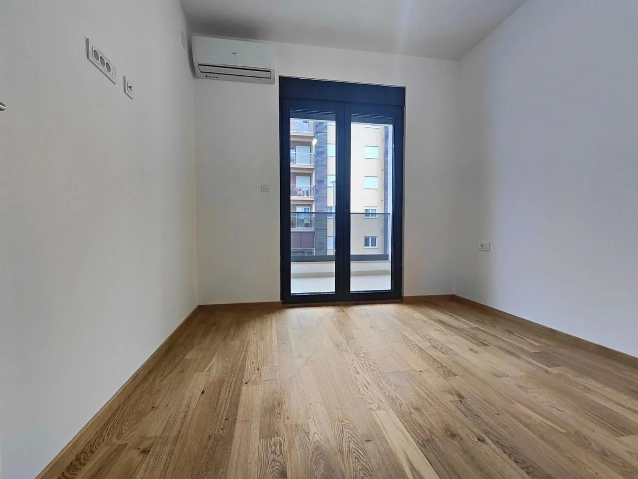Empty room with wooden flooring, air conditioning, and balcony doors.