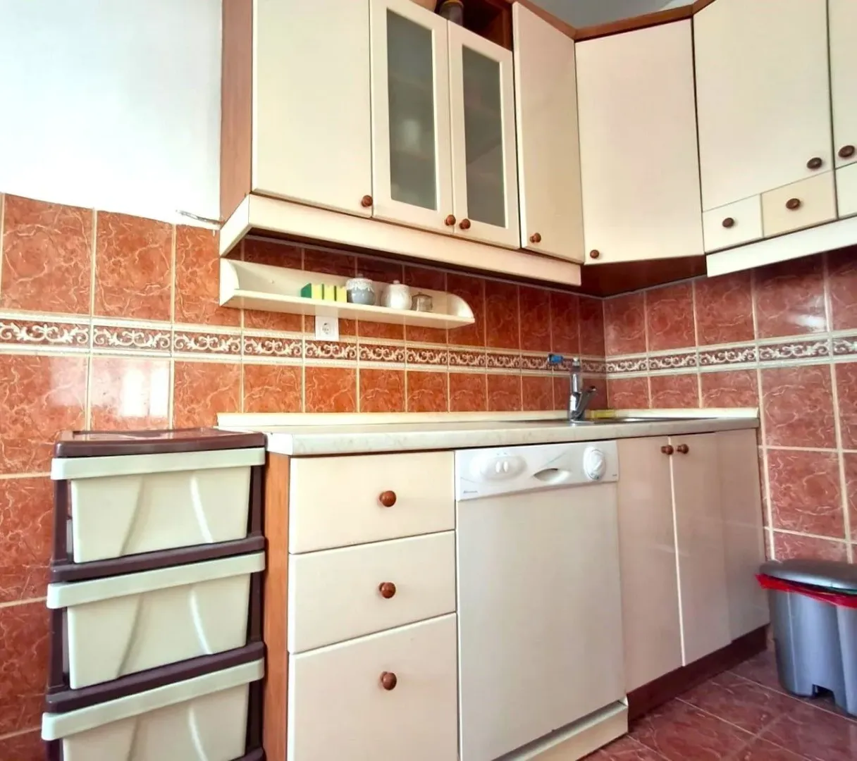 A functional kitchen featuring light cabinets and orange wall tiles.
