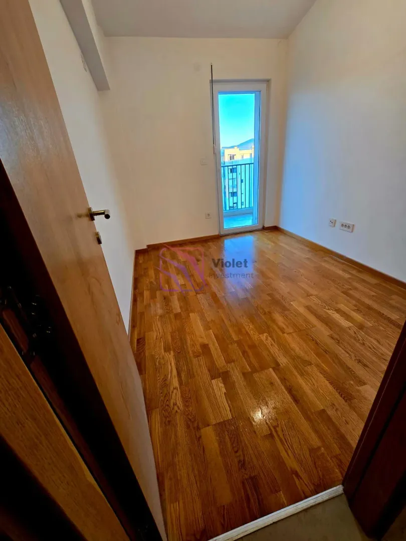 Prazna soba sa drvenim parketom i izlazom na terasu.