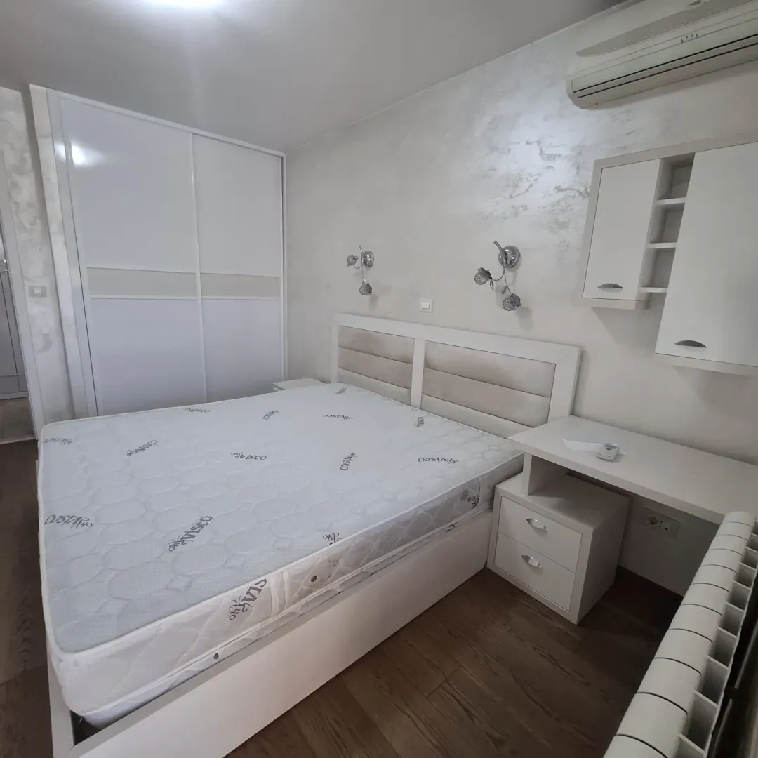 Namještena spavaća soba sa bračnim krevetom, bijelim ormarom i zidnim elementima.