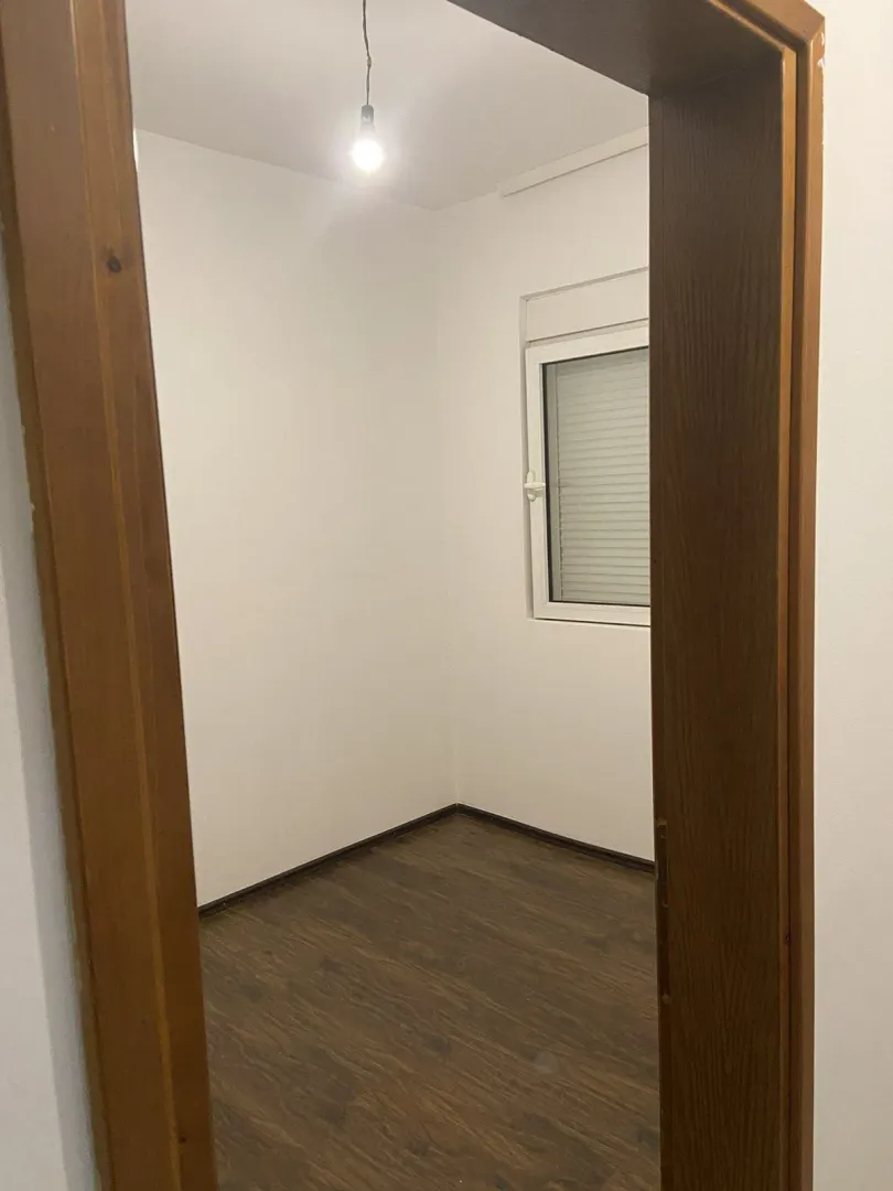 Prazna soba sa prozorom i tamnim laminatom.