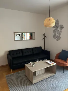Svijetla dnevna soba sa crnom kožnom garniturom, klub stolom i narandžastom foteljom. - image 2
