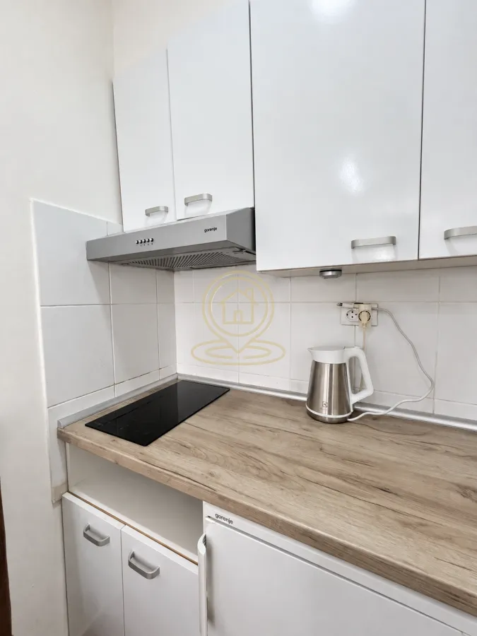 Small kitchen with white cabinets, wooden countertop and built-in cooktop.