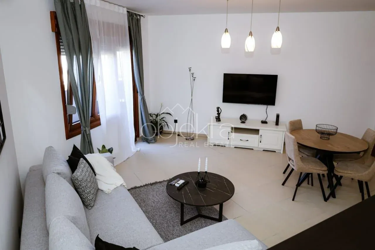 Dnevna soba sa garniturom, trpezarijskim stolom i TV komodom.