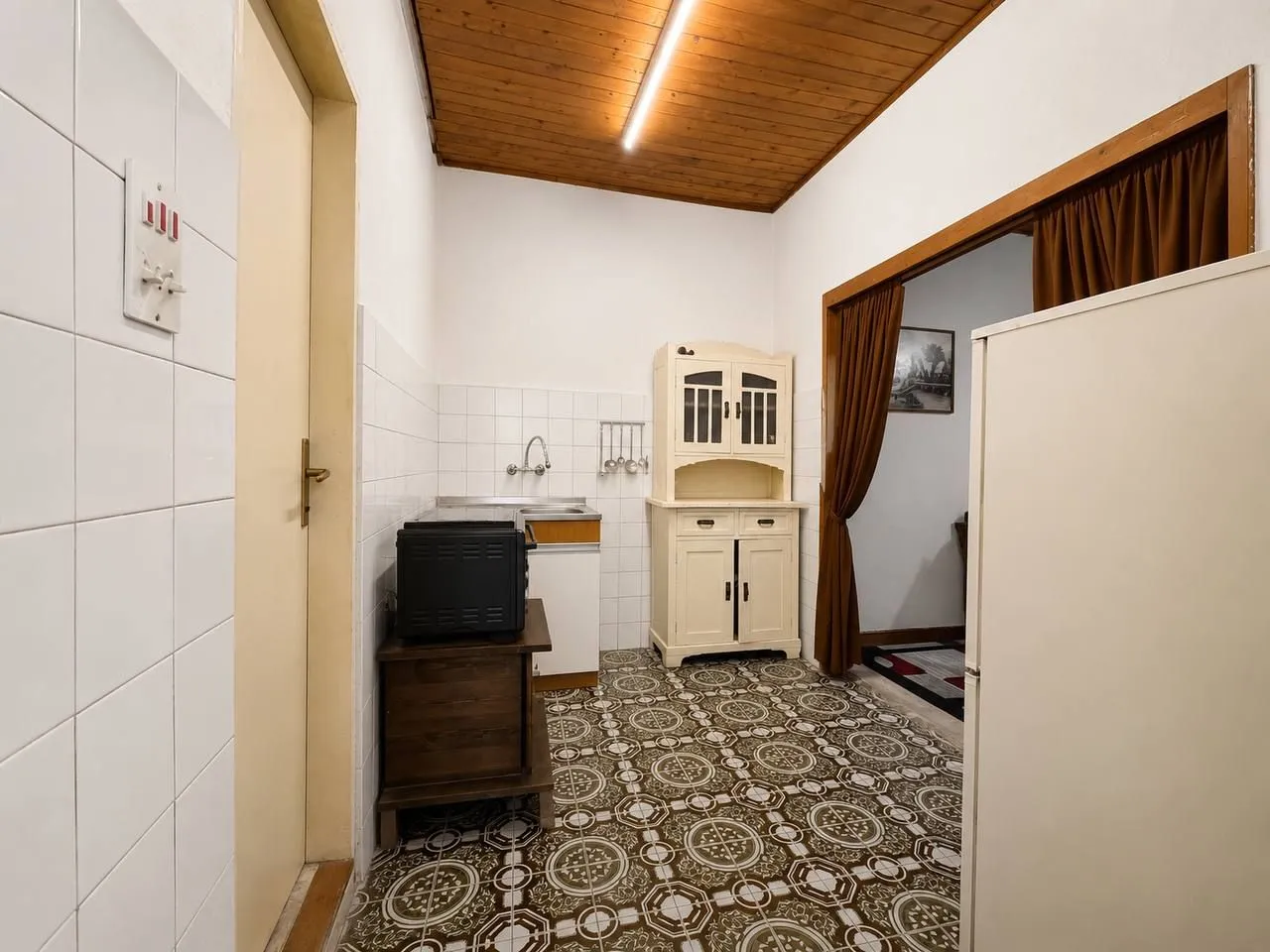 Starija kuhinja sa drvenim elementima i keramičkim pločicama.