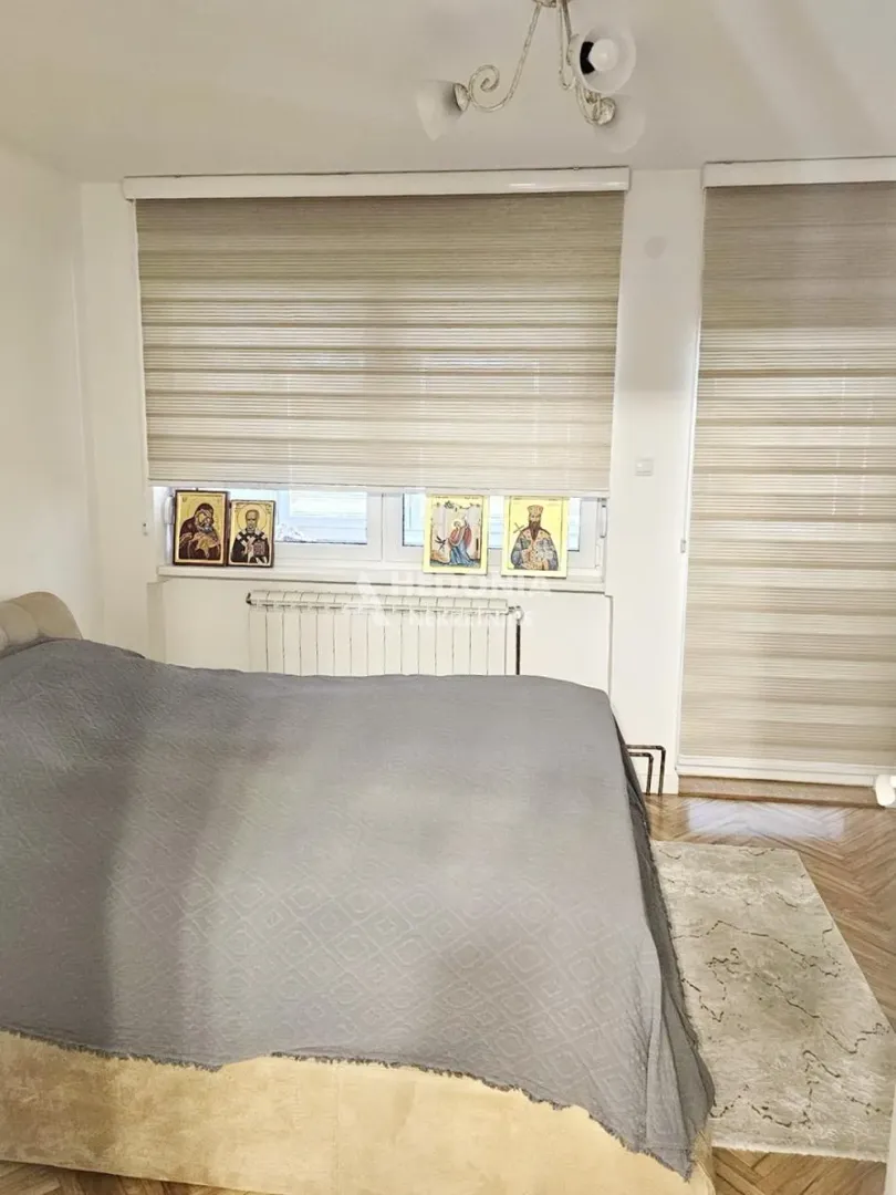 Spavaća soba sa bračnim krevetom i prozorima sa roletnama.