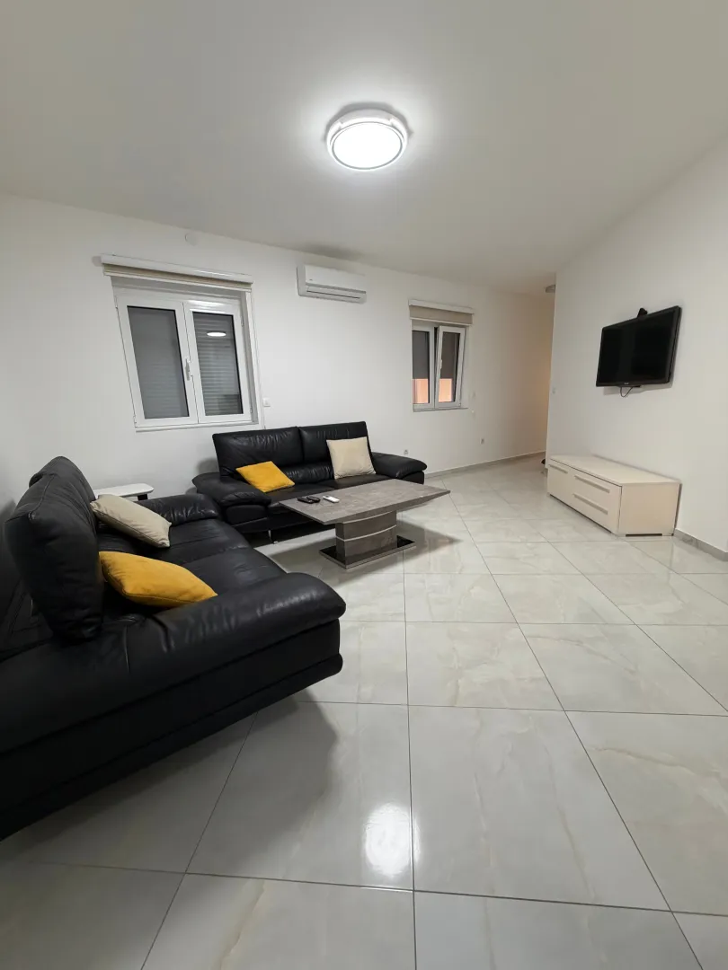 Spacious living room with black sofas and light tile flooring.