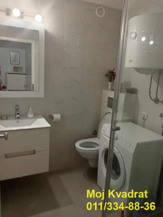 Modern bathroom with a washbasin, toilet, washing machine, and shower cabin.