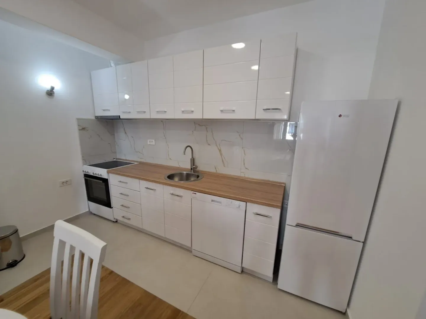 Modern white kitchen with white cabinetry, a wooden countertop, and a refrigerator.