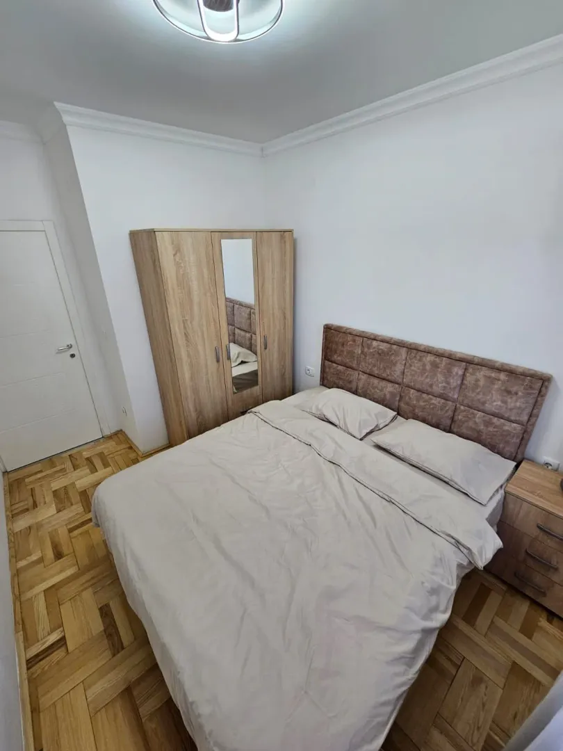 Svijetla spavaća soba sa bračnim krevetom, drvenim ormarom i parketom.