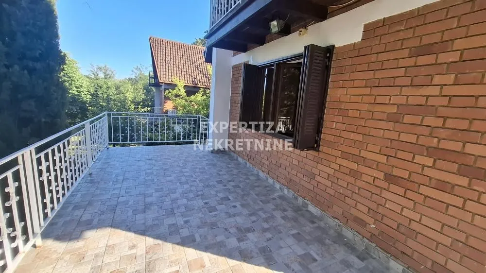 Spacious tiled terrace with metal railing and green views.