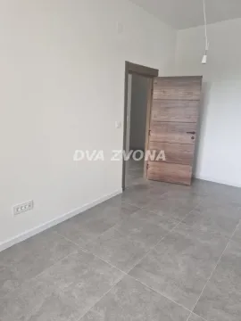 Prazna soba sa sivim keramičkim pločicama na podu i drvenim vratima. - image 4