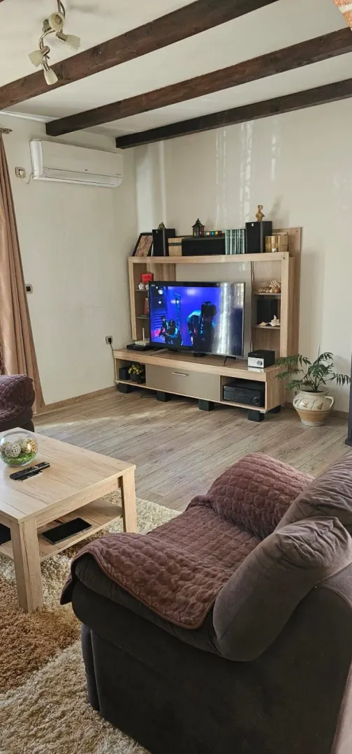 Living room with a sofa set, TV unit, and wooden ceiling beams.