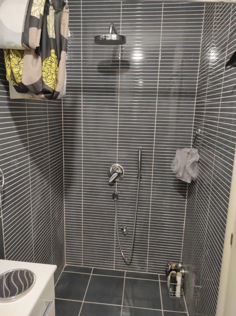 A shower cabin with grey tiles and a modern shower fixture.