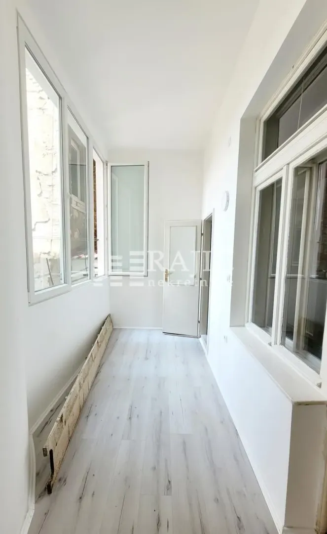 Long bright enclosed terrace with glass windows and laminate flooring.