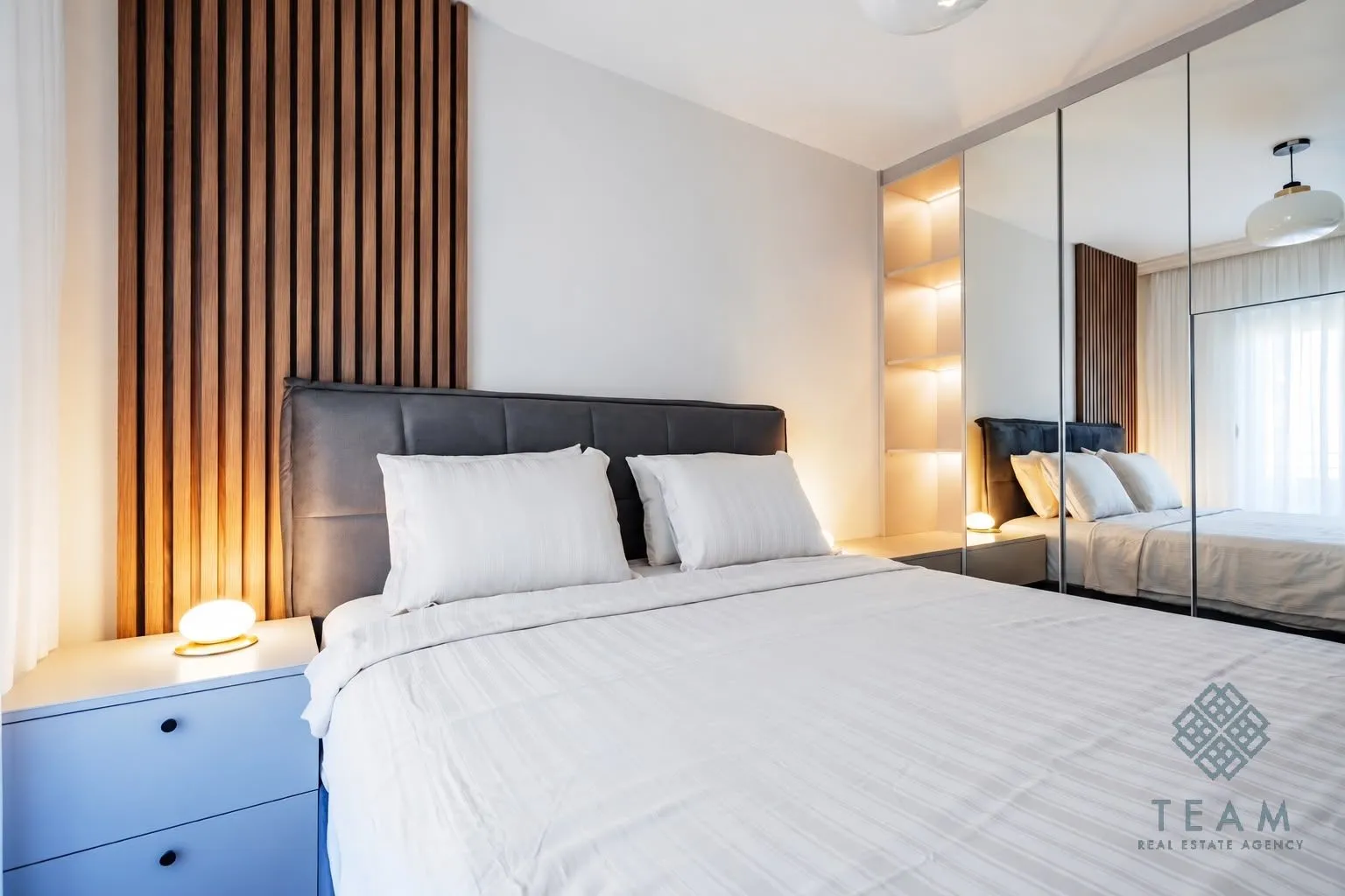 Modern bedroom with a double bed, wooden wall panel, and built-in mirrored wardrobe.