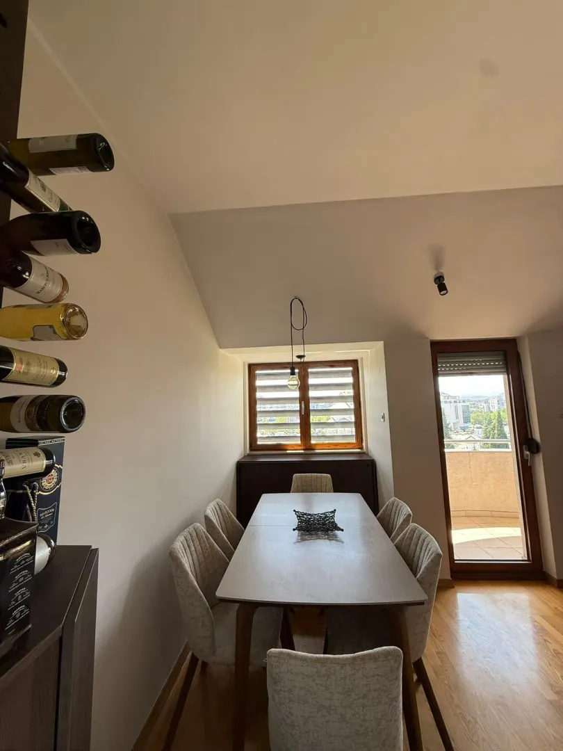 Trpezarija sa drvenim stolom i stolicama, pored zida sa stalkom za vino.