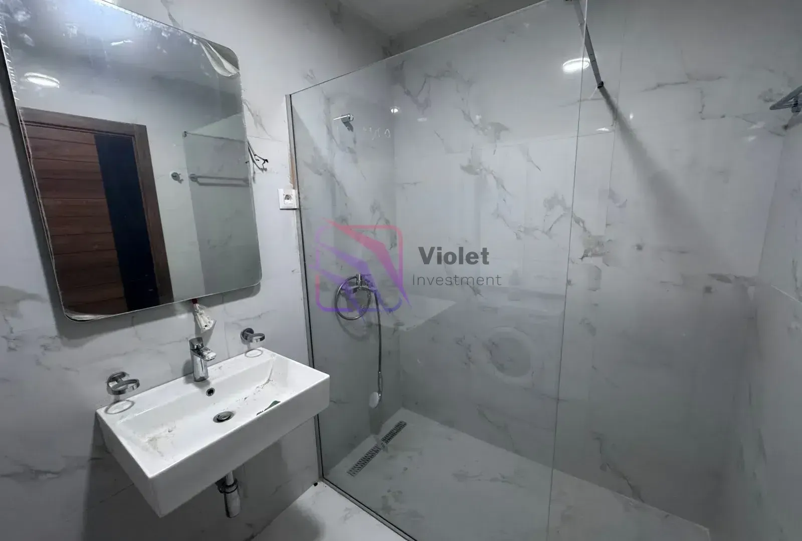 Modern bathroom with a washbasin, mirror, and a walk-in shower with a glass partition.
